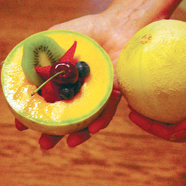 Close-up of Tasty Bites melon halves showcasing deep orange flesh and pale yellow skin held in a hand