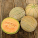 Overhead view of Tirreno melons with one half showing orange flesh and seeds on a wooden table