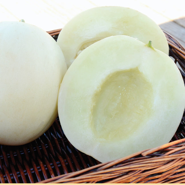 Close-up of Moonstruck honeydew melons, one whole and one halved showing pale pearly-white flesh in a wicker basket