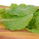 Close-up of French sorrel leaves showing large medium-green, thick spinach-like leaves on a wooden cutting board