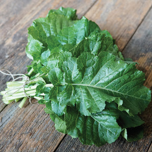 Close-up of Amara Ethiopian kale-mustard plant leaves showing crinkled green foliage on a wood surface