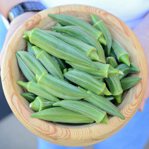 Top-down view of Jambalaya okra pods in a wooden bowl showcasing 5-ridged green, meaty pods held by a person