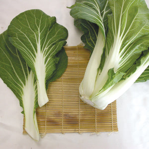 Top-down view of Joi Choi pak choi showcasing thick white stalks and dark green leaves on a bamboo mat background