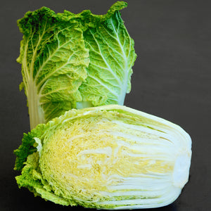 Front view of Wa Wa Tsai Chinese cabbage showing a dense barrel-shaped head and a halved cross-section on a dark background