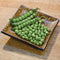 Angled top view of Canoe pea pods and shelled bright green peas on a patterned square dish set on a wooden cutting board