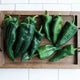 Close-up of Trident poblano peppers showcasing glossy dark green, 2-lobed ancho-style peppers on a wooden board