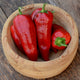 Close-up of Italian Sweet peppers showcasing glossy red, thick-walled conical fruits in a wooden bowl on a light background