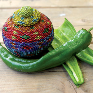 Angled view of Anaheim College 64 peppers, two long green conical fruits with one sliced to show thick walls, on a wooden surface