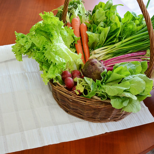 Angled view of Spring Garden seed mat with a basket of mixed vegetables including lettuce, carrots, and beets on a wooden table