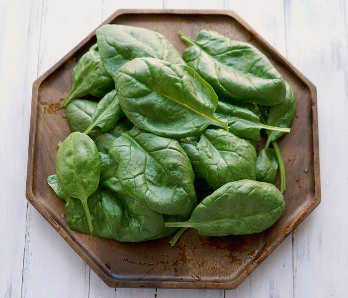 Close-up of Olympia spinach leaves on a wooden plate showing smooth dark green plain leaves