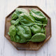 Close-up of Olympia spinach leaves on a wooden plate showing smooth dark green plain leaves