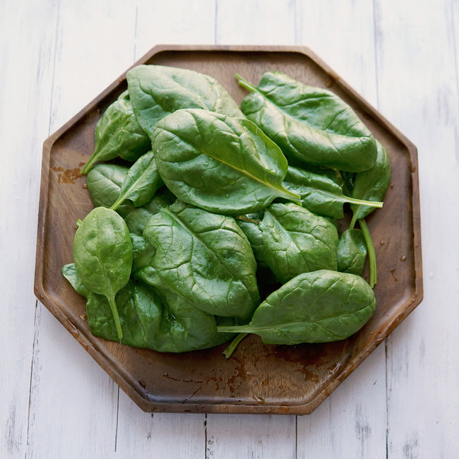 Close-up of Olympia spinach leaves on a wooden plate showing smooth dark green plain leaves