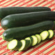 Front view of Desert summer squash (zucchini) fruits with sliced rounds showing dark green smooth skin on red striped background