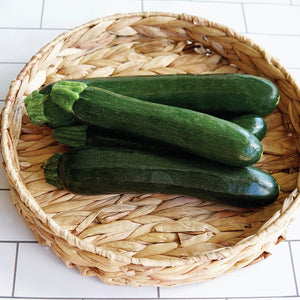 Top-down view of three Emerald Delight summer squashes with dark green smooth skin in a woven basket