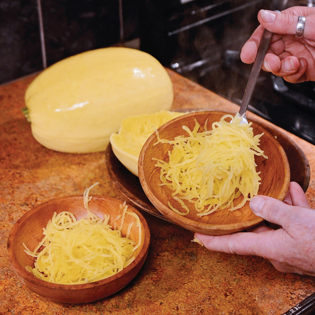 Three-quarter view of halved spaghetti squash showing stringy, spaghetti-like flesh scooped into a bowl on a cutting board
