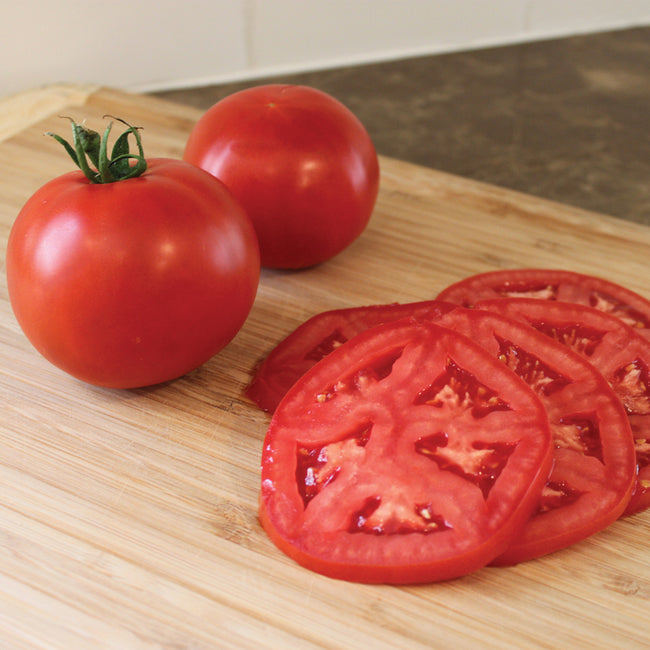 Whole and sliced Rubee Dawn tomato showcasing deep red interior and round slicing fruit on wooden cutting board