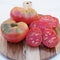 Close-up of Italian Heirloom tomato showing maroon, pleated whole fruits and sliced interior on a wooden board