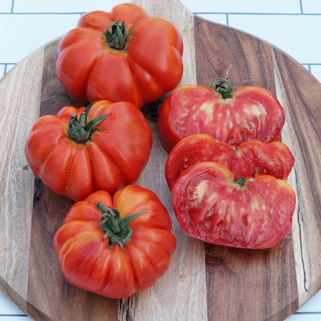Close-up of Marsalato tomatoes showcasing deeply pleated, squat shape and glossy red skin on a wooden cutting board