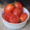 Close-up of Little Napoli tomatoes in a white ramekin showing bright crimson oval fruits and a sliced meaty interior