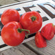 Close-up of Tasti-Lee tomatoes showing bright red, slightly flattened fruits, whole and sliced on a wooden board