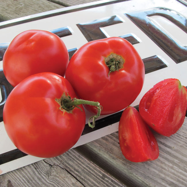 Close-up of Tasti-Lee tomatoes showing bright red, slightly flattened fruits, whole and sliced on a wooden board