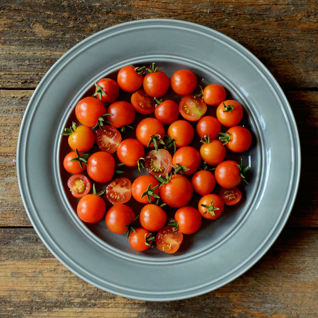 Top view of Sweet Million cherry tomatoes in a blue-gray bowl showing bright red grape-like clusters on a wooden table