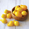 Overhead view of Yellow Pear tomatoes showing halved and whole pear-shaped yellow cherry tomatoes in a wooden bowl on a white surface
