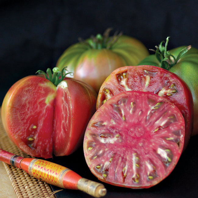 Close-up of Black Tomato sliced to show rosy-pink interior and darkened shoulders on a cutting board