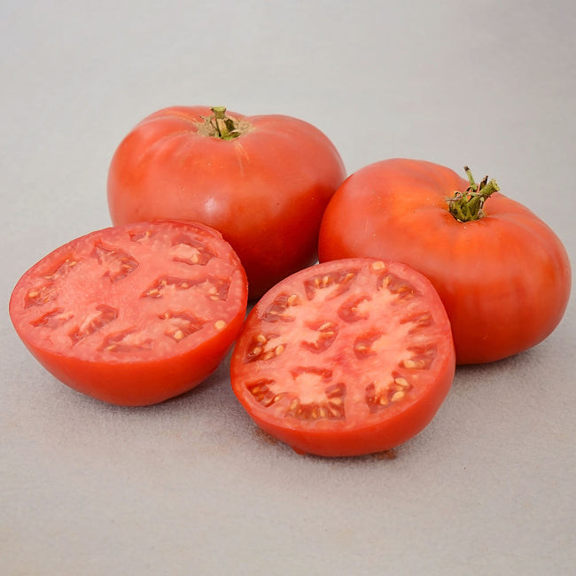 Front view of three Carmello slicing tomatoes, two whole and one halved showing deep red flesh and meaty texture on white background