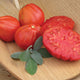 Close-up of Cuore di Bue tomato, whole and sliced, showing dense orange-red flesh and meaty texture on a wooden board