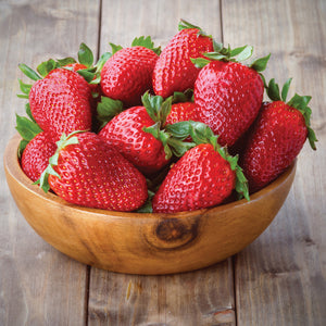 Close up of Chandler strawberries showing large glossy red berries in a wooden bowl on a wooden table