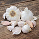 Close-up of two Silver White garlic bulbs and several loose cloves showing pure-white wrappers and plump cloves on a rustic wooden surface