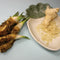 Front view of horseradish bare roots with green shoots and grated horseradish in a white dish on pale blue background