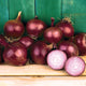 Front view of Southern Belle Red onion bulbs with deep ruby skins and a sliced bulb on a wooden shelf