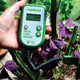 Front view of Digital 3-Way Analyzer showcasing its green handheld design with garden plants in background