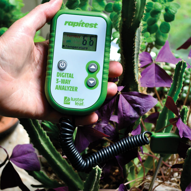 Front view of Digital 3-Way Analyzer showcasing its green handheld design with garden plants in background