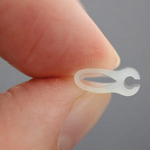 Close-up of translucent silicone grafting clip held between thumb and forefinger showing U-shaped design against white background