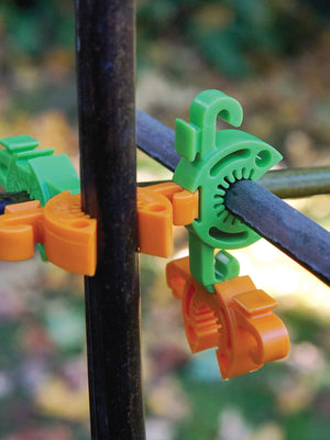 Close-up of C-Bite stake clips in tangerine snapped to a black garden stake showcasing connector design and netting hook