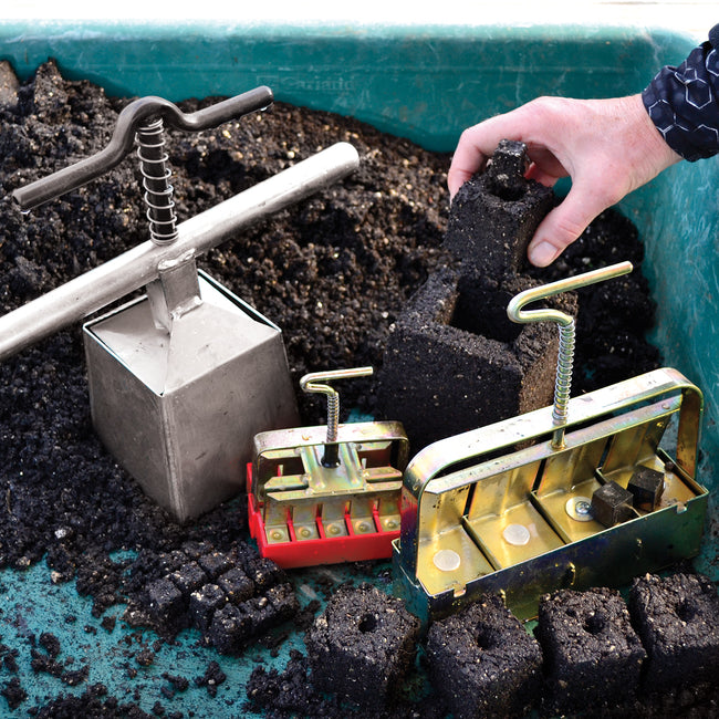 Front view of 4 inch soil blocker showing wooden handles and square block mold with potting soil background