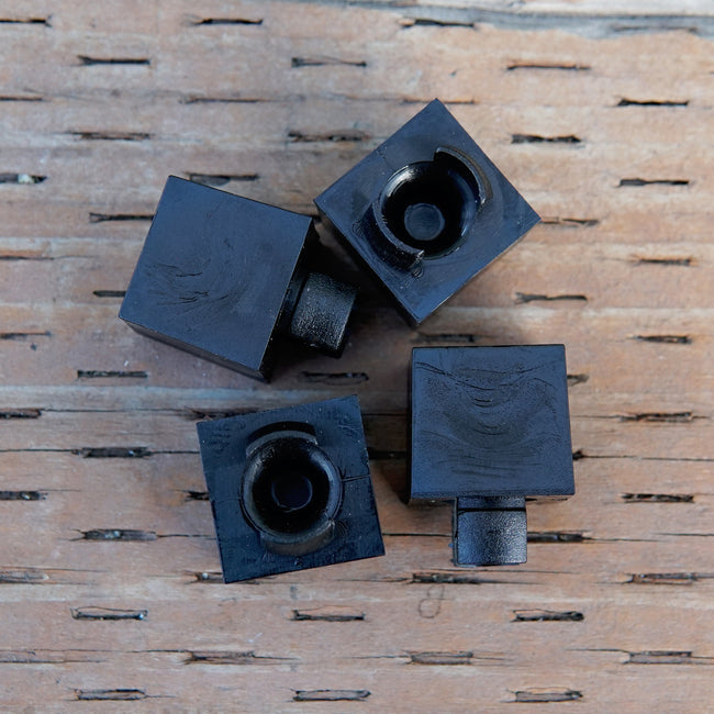 Top-down view of four black cube seed-starting inserts showing hollow dimpled bottoms and small tabs on a wooden surface
