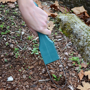 Angled view of Garden Ninja weeding tool showing thin stainless-steel blade cutting a small weed in a mulch garden bed